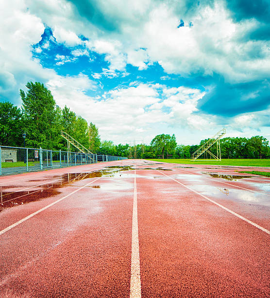 Wet red running track after rainfall Wet red running track after brief Summer rainfall. Tee sky is clearing up. Bleachers are on either side and trees line the track behind. Photographed in a public city park in Montreal, Canada. all weather running track stock pictures, royalty-free photos & images