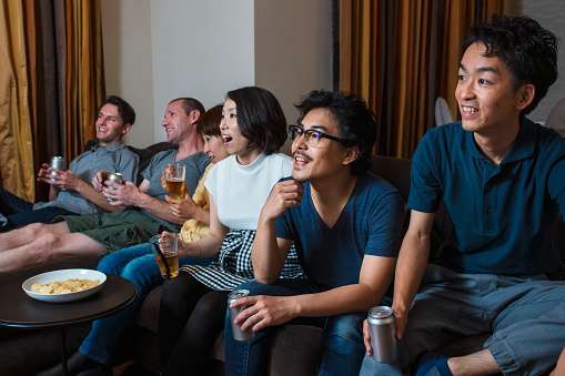 Multiracial group of friends sat drinking beer watching a TV together. Kyoto, Japan. May 2016