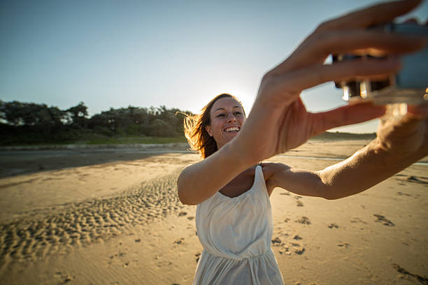 giovane donna in spiaggia scatta selfie usando fotocamera indossabile - australia photographing camera beach foto e immagini stock