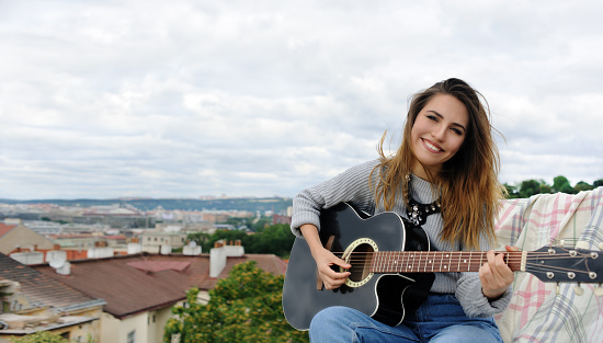 Girl playing the guitar on the background of the park on the roof