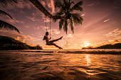Carefree woman swinging above the sea at sunset beach.