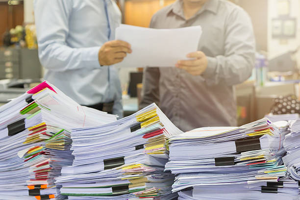 istock Pile of unfinished documents on office desk with businessman background 579249640