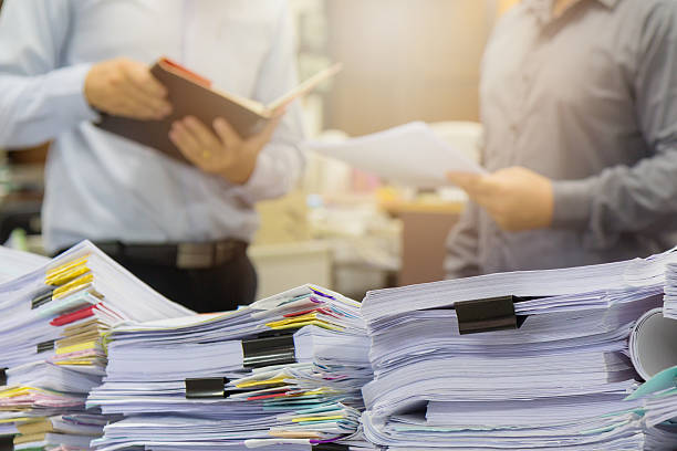 istock Pile of unfinished documents on office desk with businessman background 579249716