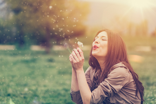Young woman blowing out dandelion
