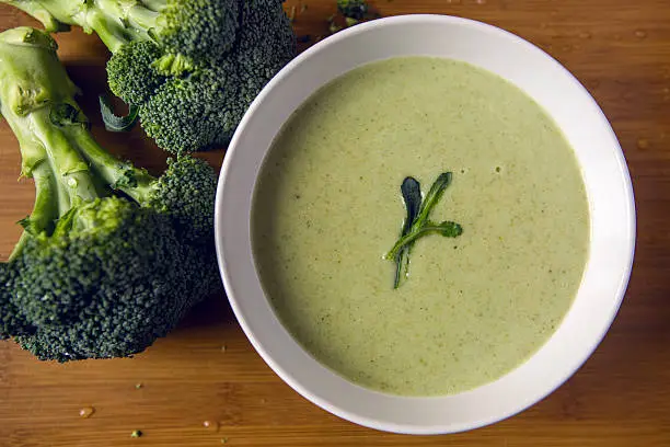 cream of broccoli soup in a white bowl on a wooden table with slices of the stems