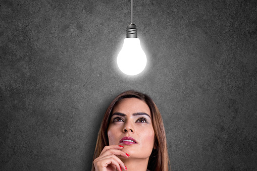 Businesswoman looking at glowing light bulb. The glowing light bulb is a symbol of success.