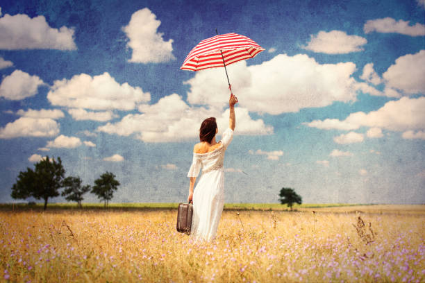 photo of the beautiful young woman with suitcase and umbrella in the field