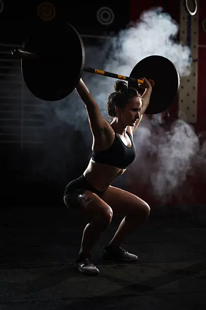 Sweating girl lifting heavy barbell