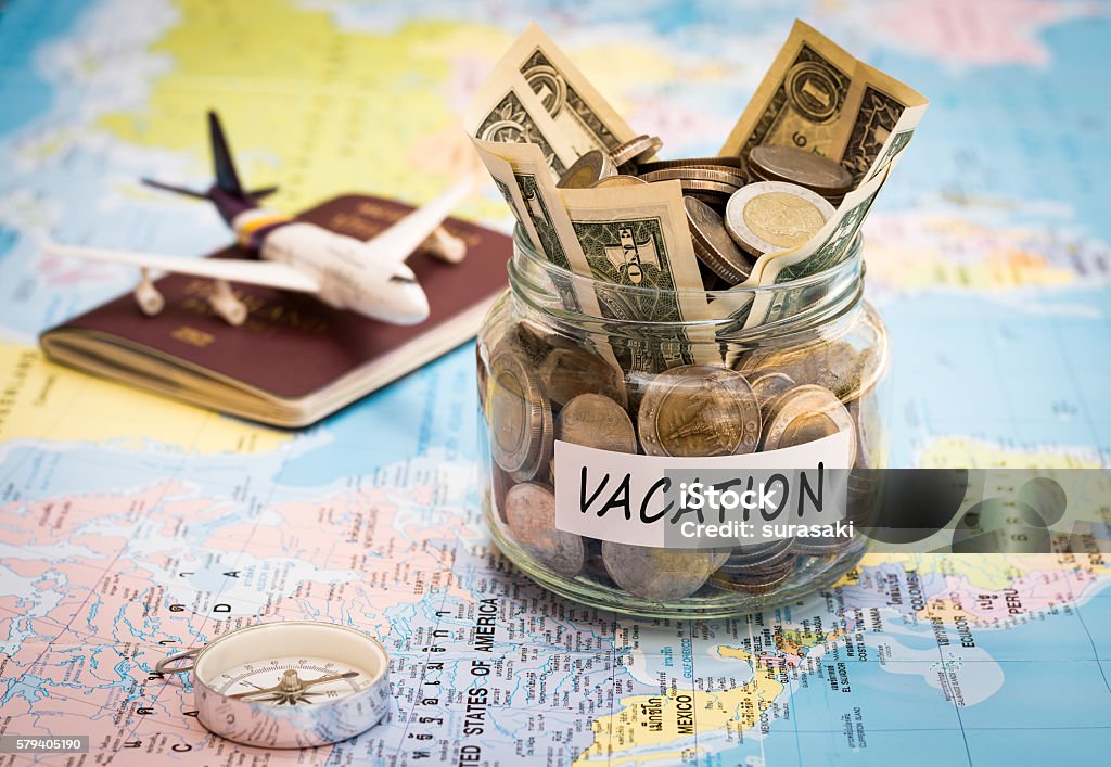 Vacation budget concept with compass, passport and aircraft toy Vacation budget concept. Vacation money savings in a glass jar with compass, passport and aircraft toy on world map Budget Stock Photo