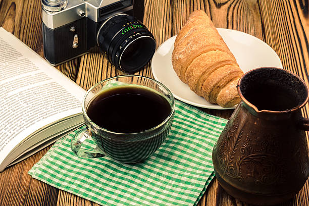 istock Cup black coffee on napkin, croissant, book, vintage camera 579405924