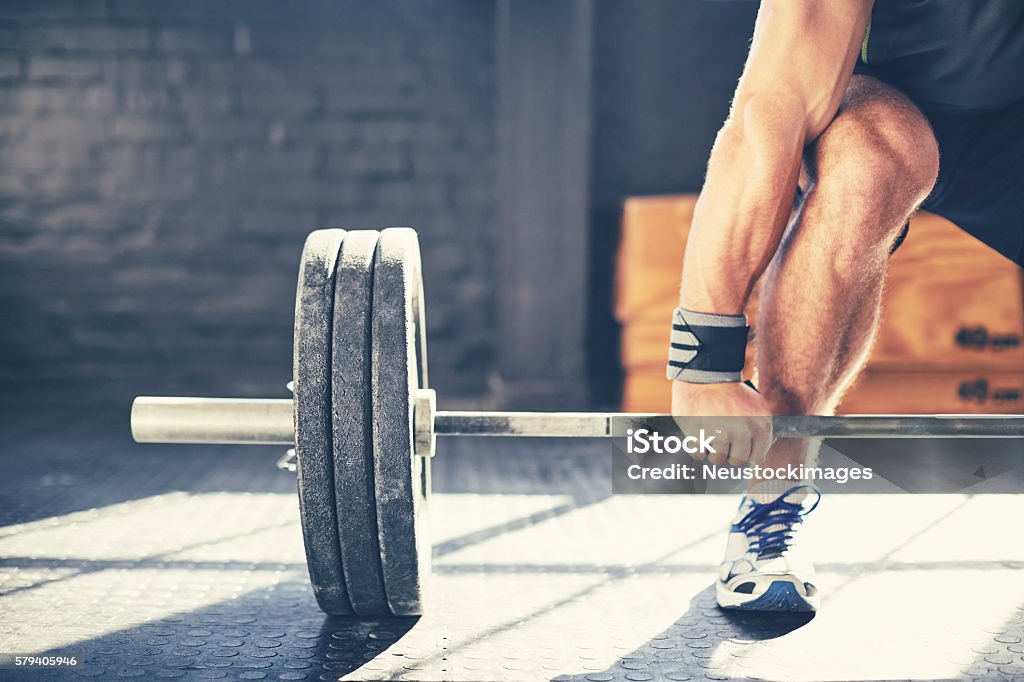 Cropped image of muscular man deadlifting barbell in gym Cropped image of muscular man deadlifting barbell. Determined male is exercising in brightly lit gym. Sunlight is falling on floor creating shadows. Barbell Stock Photo