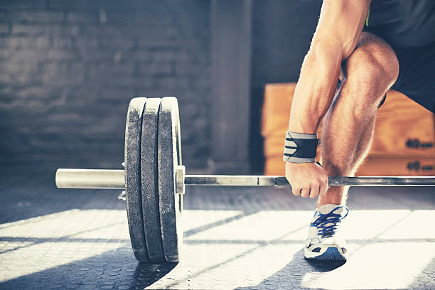 Cropped image of muscular man deadlifting barbell in gym Cropped image of muscular man deadlifting barbell. Determined male is exercising in brightly lit gym. Sunlight is falling on floor creating shadows. lift weights stock pictures, royalty-free photos & images