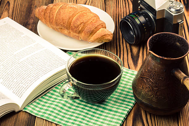 istock Cup black coffee with croissant, book, turkish coffee pot, camera 579405992