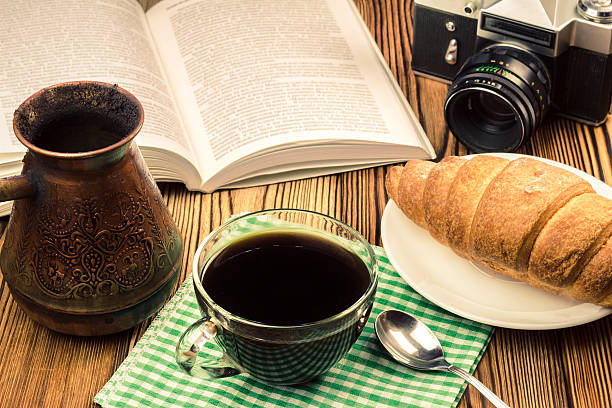 istock Cup black coffee with croissant, book, turkish coffee pot, camera 579406084