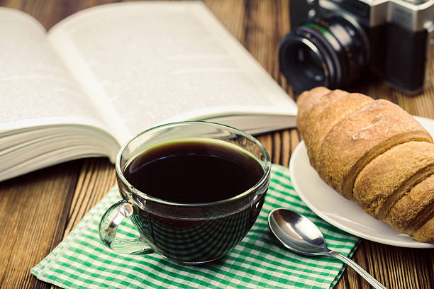 istock Cup black coffee with croissant, book, vintage camera 579406142