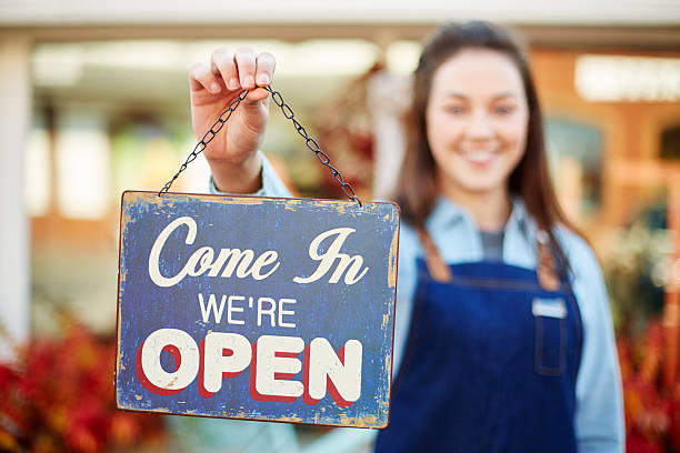 istock Smiling florist holding up sign saying come in we're open 579407938