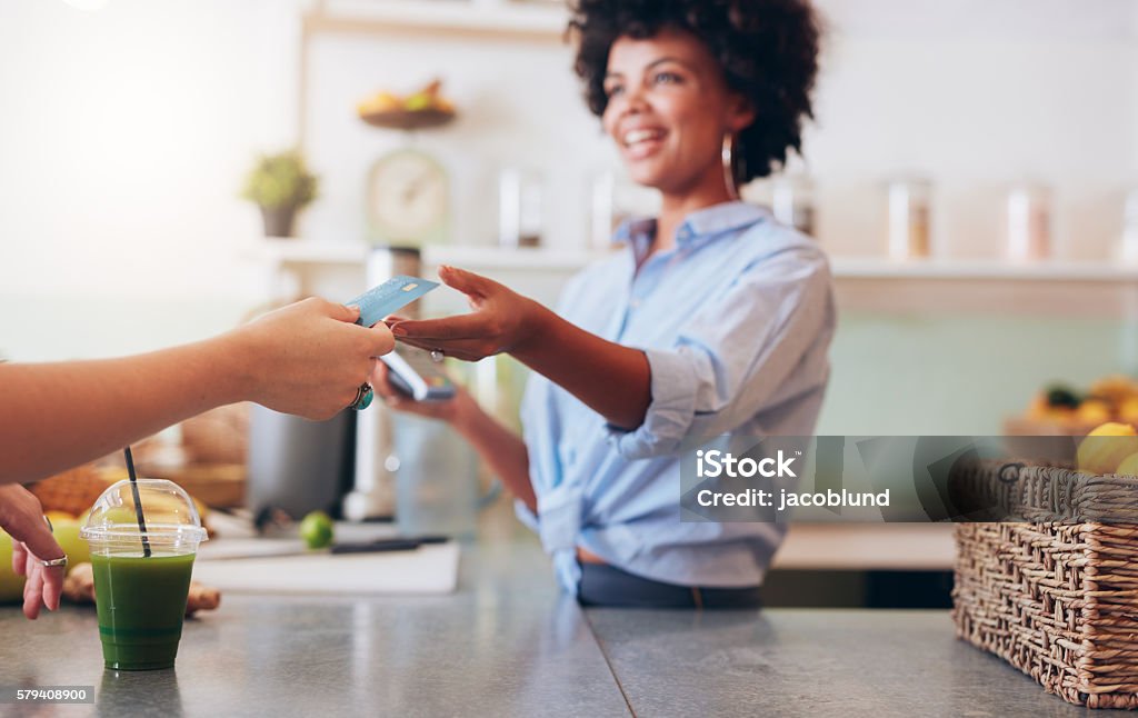 Female employee taking payment from customer Cropped shot of female employee taking payment from customer, focus on female hands giving credit card for juice bar payment. Paying Stock Photo