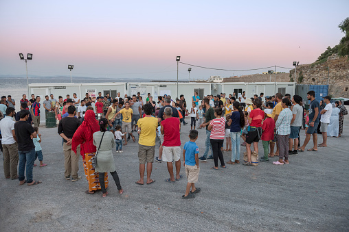 Chios, Greece - July 21, 2016: A group of refugees and volunteers (from the Norwegian NGO Drop in the Ocean and People's Street Kitchen) are dancing (or standing watching) and clapping hands to traditional Syrian music (from a boom box) on a hot summer evening at sunset in the Souda refugee camp on the Greek Island of Chios in the Aegean Sea.