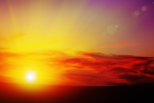 Behind red and gold-tinged clouds, the sun glows brightly. It is either sunrise or sunset on a beautiful day. Beautiful natural background or simply ample copy space.