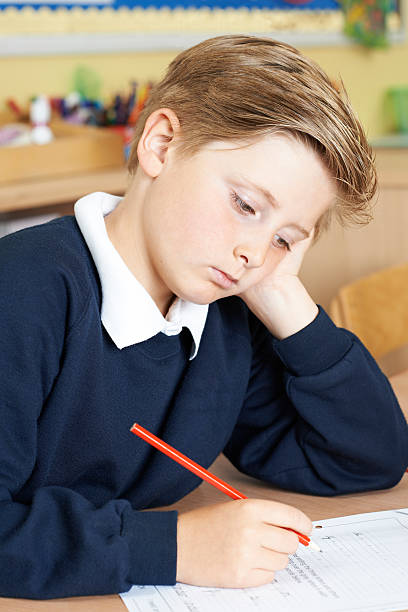 istock Bored Male Elementary School Pupil At Desk 579431934