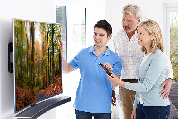 Man Demonstrating New Television To Mature Couple At Home Man Demonstrating New Television To Mature Couple At Home installing tv stock pictures, royalty-free photos & images