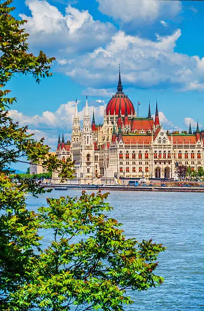 Hungarian parliament building at danube river in budapest city hungary blue sky with clouds and green tree leaves