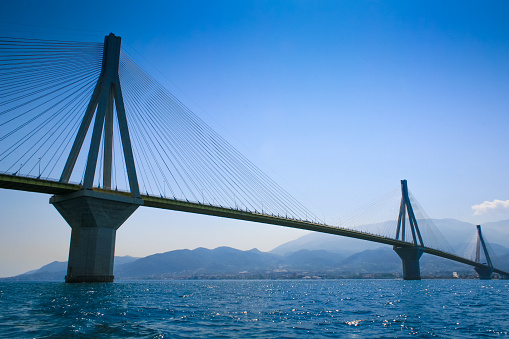 The Antirrio Suspension Bridge, Patras, Gulf of Corinth, Greece,  in calm water with blue sea and sky. The  bridge spans from the town of Rio on the Peloponnese peninsula to Antirrio on mainland Greece.