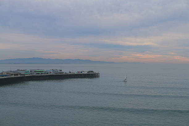 Sailboat and pier in Santa Cruz, CA Sailboat in calm waves near the Santa Cruz Pier in Monterey Bay, California on an overcast evening. monterey bay stock pictures, royalty-free photos & images