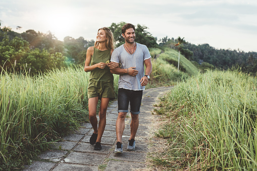 Outdoor shot of young couple in love walking on pathway through grass field. Man and woman walking along tall grass field.