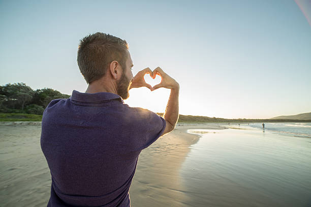 istock Caucasian male frames sunset on beach into heart shape 579734050