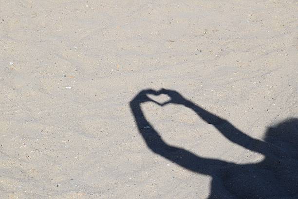 istock Shadow of heart made with hands on the sand 579737604