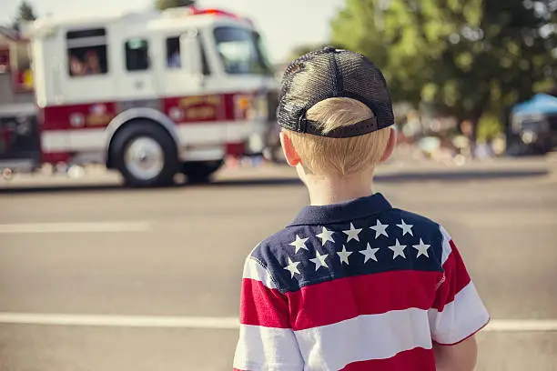 A rear view of a boy watching a fire engine drive by during a parade procession during an Independence Day parade in a small town in the USA.