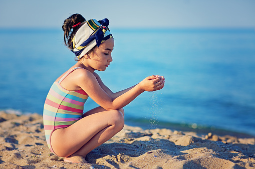 Small girl is standing on the beach and playing with the sand.