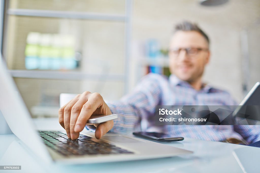 Entering system Hand of man with cellphone pressing laptop key Addict Stock Photo