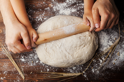 Father and child hands making the dough with flour, rolling pin and wheat ears on rustic wooden table top view. Homemade pastry for bread or pizza. Bakery background.