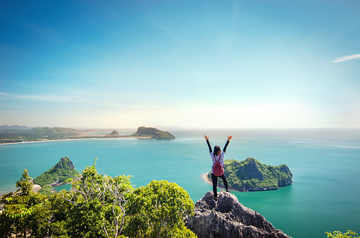 Freedom traveler woman standing with raised arms on the top of mountain at Khao Lom Muak and enjoy the beautiful of seascape, travel, freedom, Thailand.