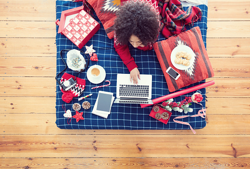 High angle view of woman lying on the stomach on a bed and using a laptop. Winter scenery.