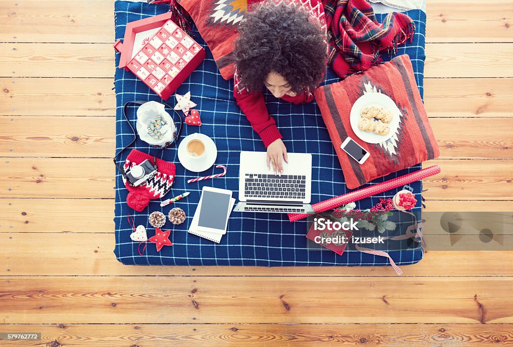 Woman lying on bed and using laptop High angle view of woman lying on the stomach on a bed and using a laptop. Winter scenery. Adult Stock Photo