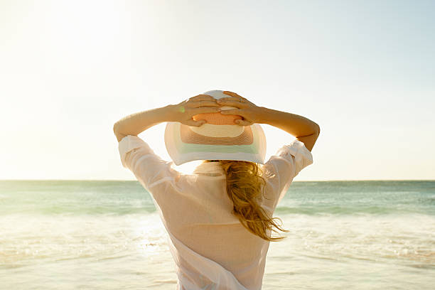 I am completely mesmerized Rearview shot of a young woman standing on the beach sun hat stock pictures, royalty-free photos & images