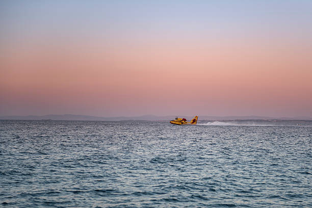 Chios, Greece - July 25, 2016: A devastating fire startet 1 AM on July 25th in the forests in the south of the Greek Island of Chios, including large areas where the precious Mastic tree is cultivated. At sunset, almost 24 hours later, the firefighting continued, including using airtankers for aerial firefighting. The image shows a Bombardier 415 Superscooper aircraft touching the sea to load the watertank, as the sun sets in the Aegean sea.
