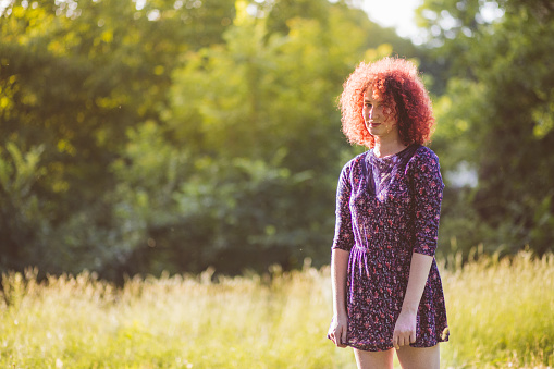 Summer outdoor scene of woman with big curly red hair styled in floral designed dress.
