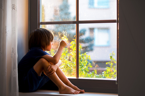 Sad child, boy, sitting on a window shield, watching the sunset