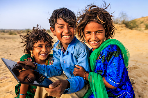 Group of happy Gypsy Indian children using digital tablet in desert village, Thar Desert, Rajasthan, India.