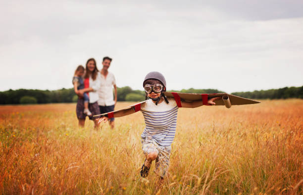 niño juguetón con alas en gorra de aviador y gafas voladoras en el campo - family adult portrait cheerful fotografías e imágenes de stock