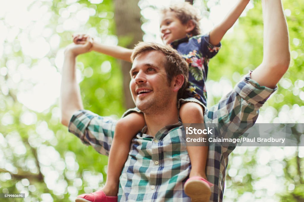 Father carrying son on shoulders below trees  2-3 Years Stock Photo