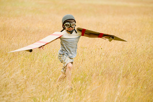 Boy running with wings and aviators cap and flying goggles in field