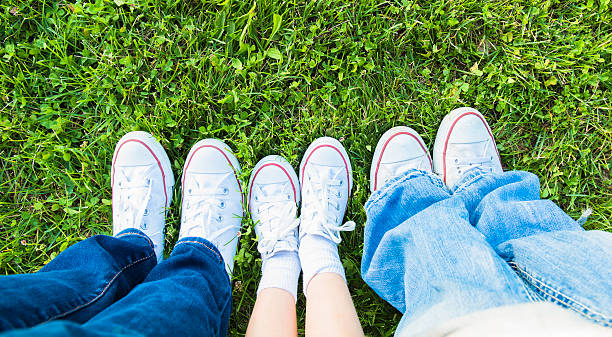 Family of three, laying down in the grass outside with a view of all the tennis shoes together.