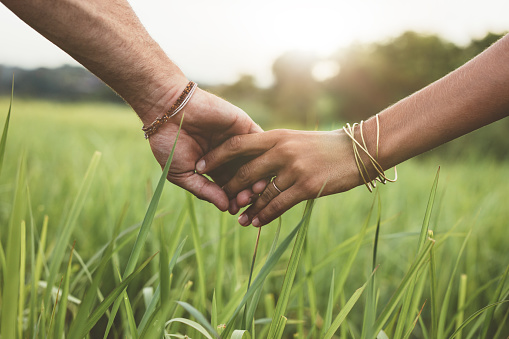Shot of romantic couple holding hands in a field. Close up shot of man and woman with hand in hand walking through grass field.