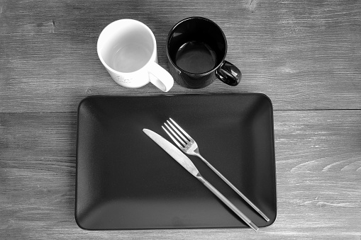 Simple clean design. Laconic black and white set of dishware with knife and fork on a wooden table. Black and white. Copy space.