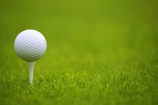 White Golf ball on tee on green grass of golf course